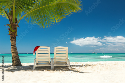 Fototapeta Naklejka Na Ścianę i Meble -  Santa's hat and sun loungers on the tropical beach