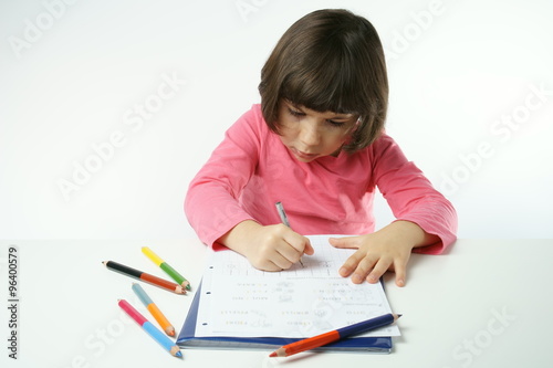 little girl is doing homework on a white background, dressing a pink shirt
