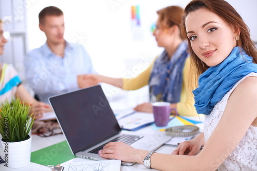 Portrait of attractive female designer sitting on desk in office
