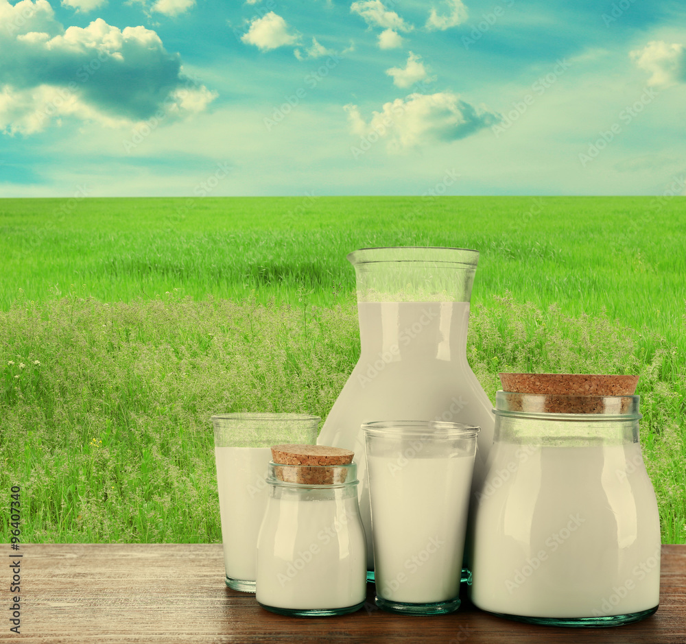Pitcher, jars and glasses of milk on field background Pitcher, jars and glasses of milk on field background
