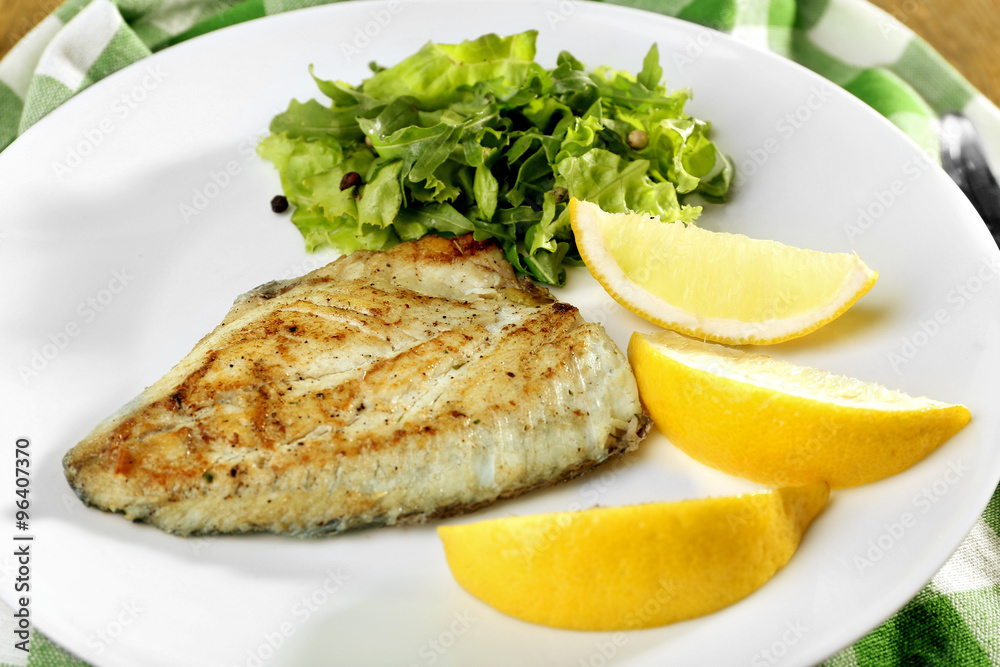 Dish of fish fillet with greens and lemon on plate close up Dish of fish fillet with greens and lemon on plate close up