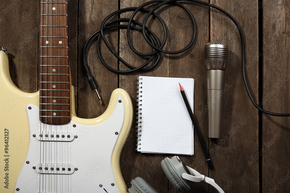 Naklejka premium Electric guitar with headphones and microphone on wooden background