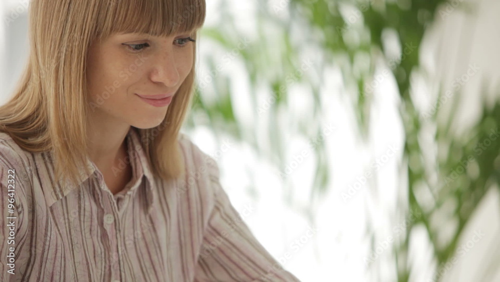Beautiful young woman using laptop writing in notebook and smiling at camera