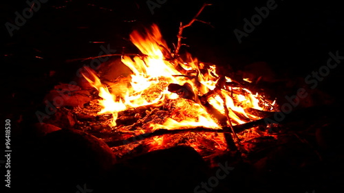 Flames of a cozy campfire flicker in a light breeze against a dark night photo