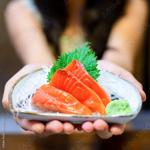 Woman hands holding white plate with Salmon sashimi