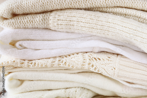 Stack of white cozy knitted sweaters on a wooden table 
