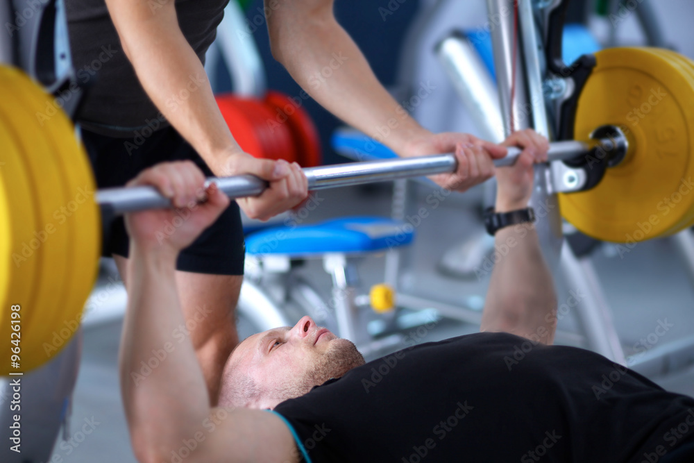 Fototapeta premium Young man lifting the barbell in gym with instructor