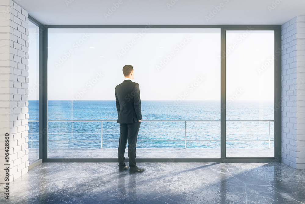 Fototapeta premium Businessman in empty loft room with big window in floor and ocea