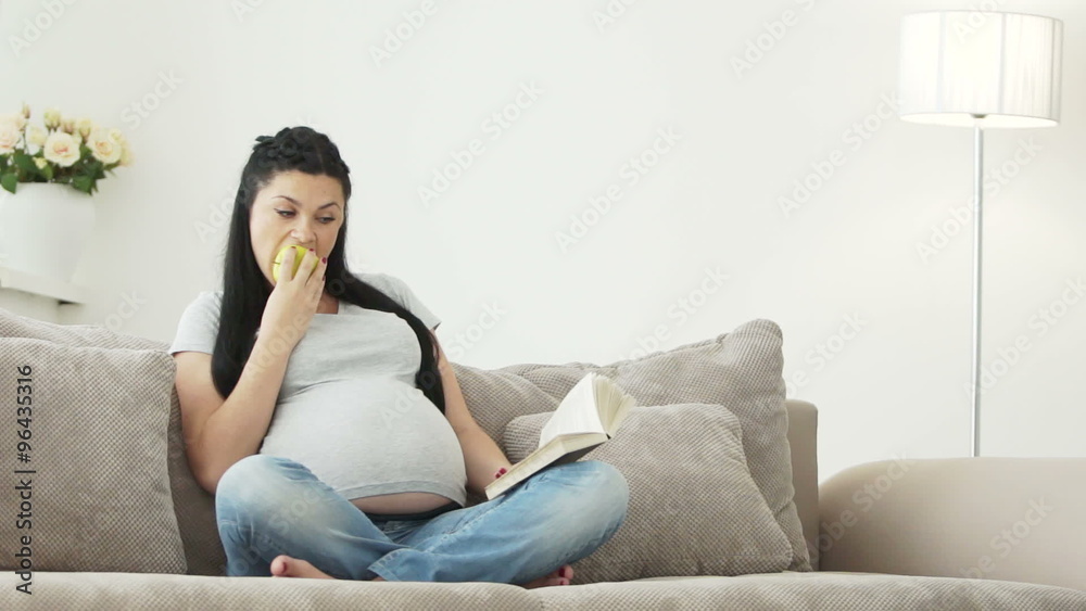 Pregnant woman eating apple and reading a book with a smile Pregnant woman eating apple and reading a book with a smile