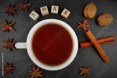 Christmas background. Christmas cup with tee, nuts, cinnamon, anise stars and card X-MAS. Merry X-MAS concept.