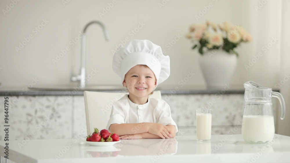 Little boy chef sitting at table and smiling Little boy chef sitting at table and smiling