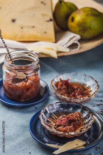 Small jam dishes with rose petal jam, pears and a big piece of cheese on a turquoise table-cloth.