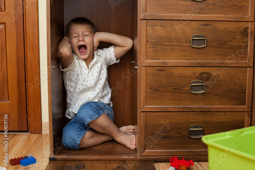 little boy hiding in a cupboard and crying
