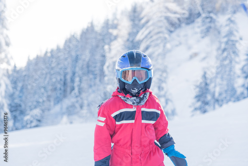 Little seven years old skier in red suit blue helmet and goggles