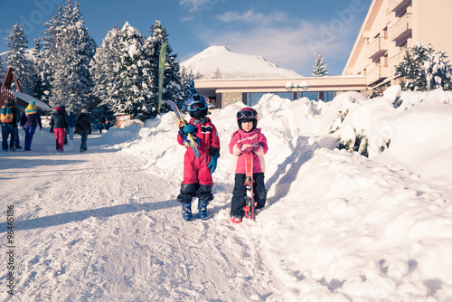 Two little siblings skiers standing together with skies wearing