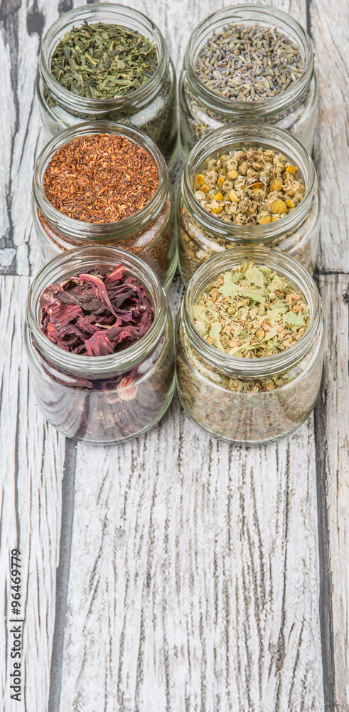 Dried herbal tea lavender, chamomile, linden flower, hibiscus, rooibos, Japanese green tea in mason jar over wooden background Dried herbal tea lavender, chamomile, linden flower, hibiscus, rooibos, Japanese green tea in mason jar over wooden background