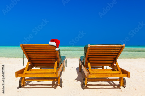 Chairs on tropical beach and Santa Claus red christmas hat