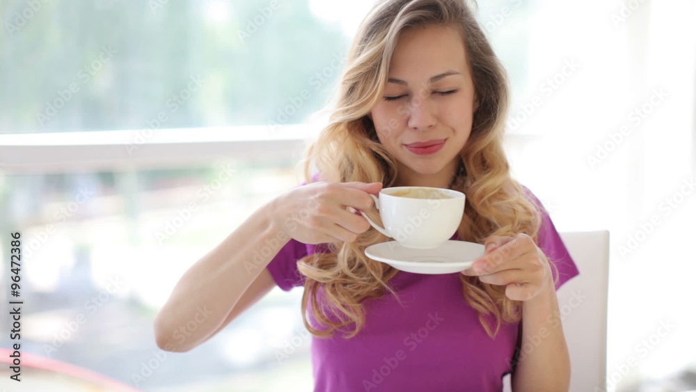 Pretty young woman sitting at table enjoying coffee and smiling at camera