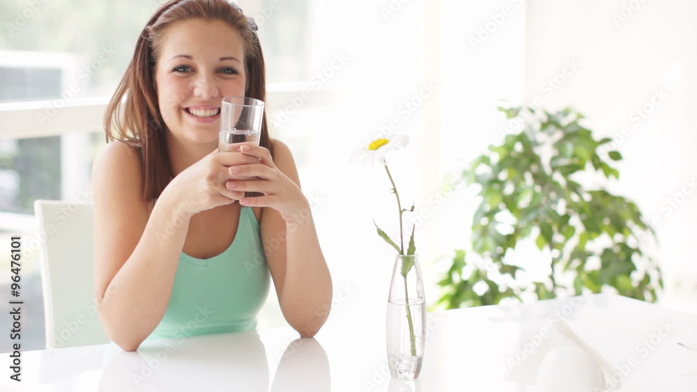 Pretty girl sitting at table holding glass of water smiling and laughing Pretty girl sitting at table holding glass of water smiling and laughing