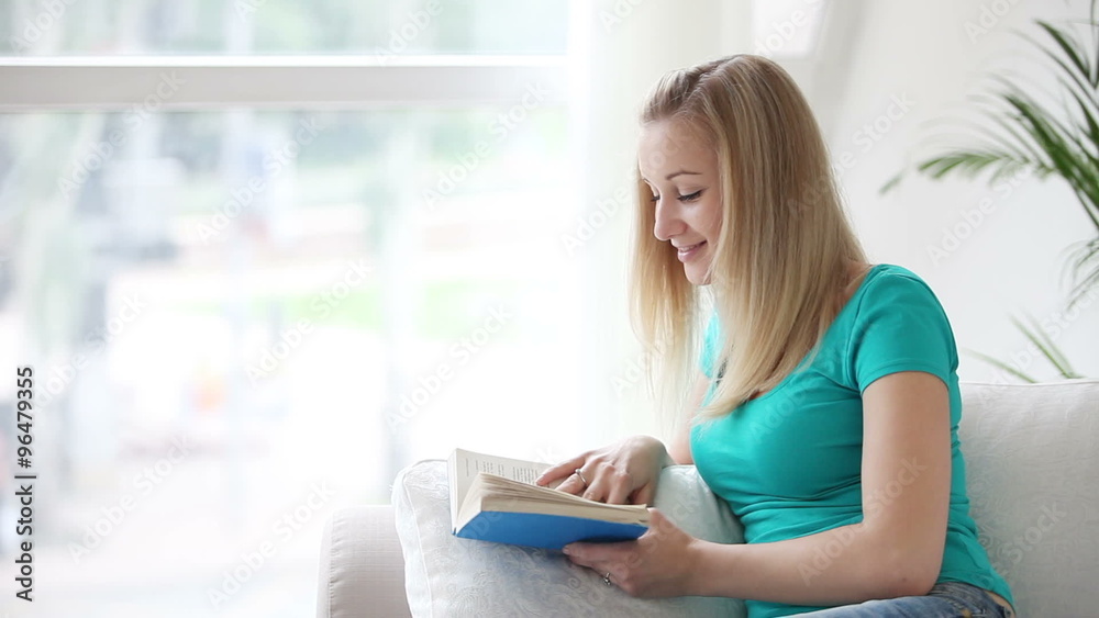 Attractive young woman relaxing on couch with book looking at camera and smiling Attractive young woman relaxing on couch with book looking at camera and smiling