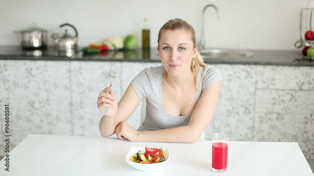 Pretty young woman sitting at kitchen table eating vegetable salad and smiling Pretty young woman sitting at kitchen table eating vegetable salad and smiling