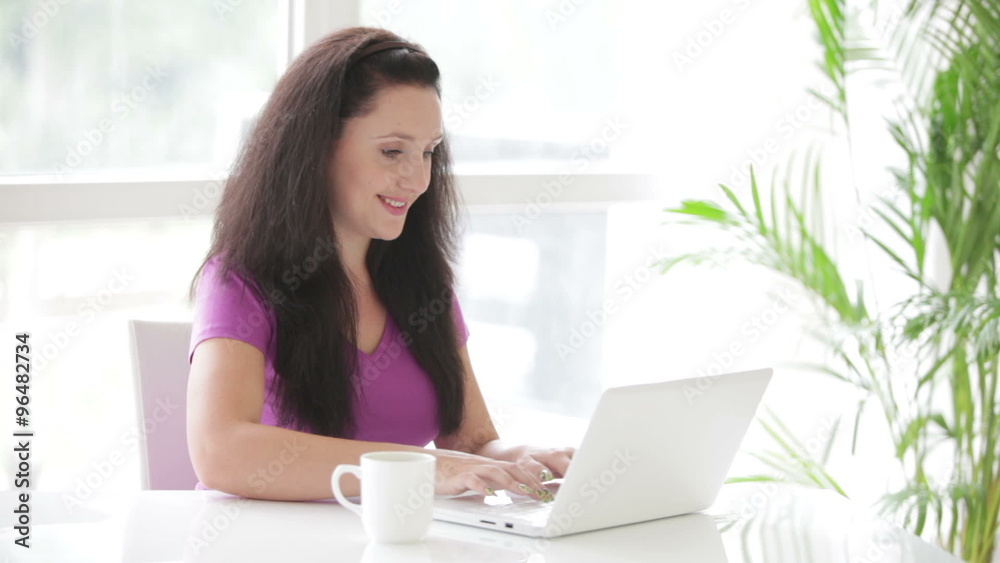 Brunette young woman sitting at table with laptop drinking coffee ad looking at camera smiling Brunette young woman sitting at table with laptop drinking coffee ad looking at camera smiling