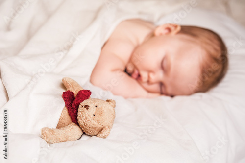 a sweet baby sleeping on a blanket with his bear