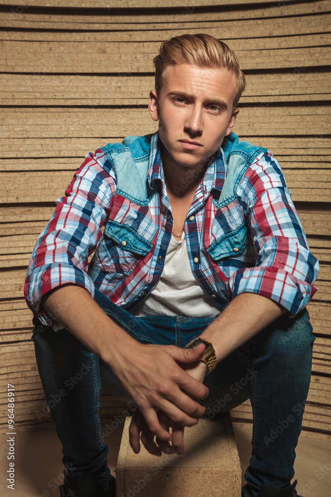 male sitting on a box in wooden studio background while touching