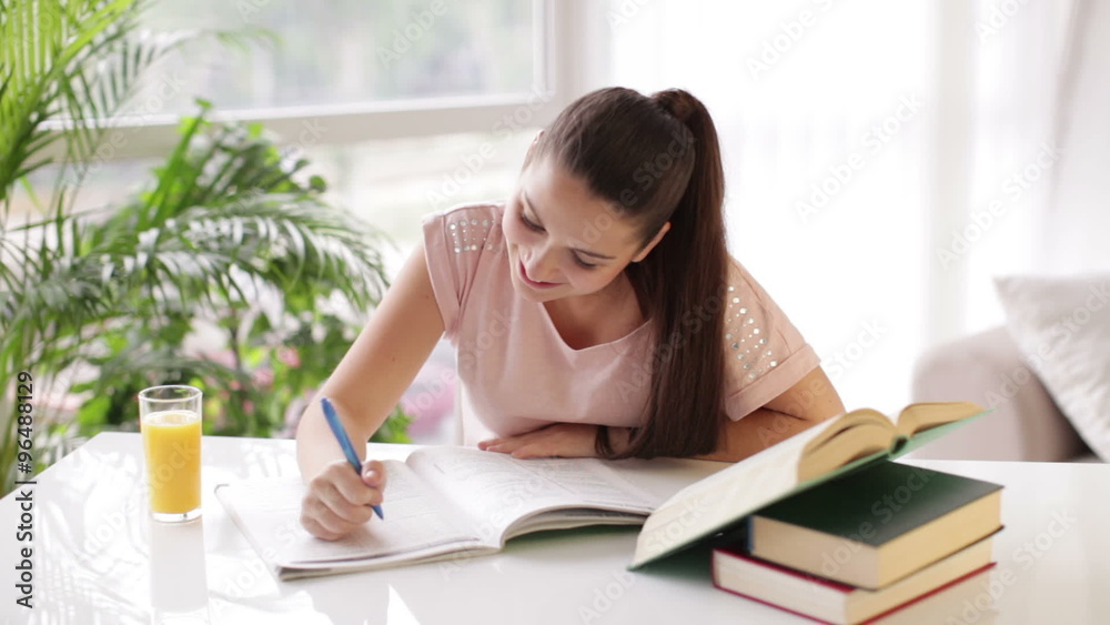 Cheerful student girl studying at table with books drinking juice and smiling