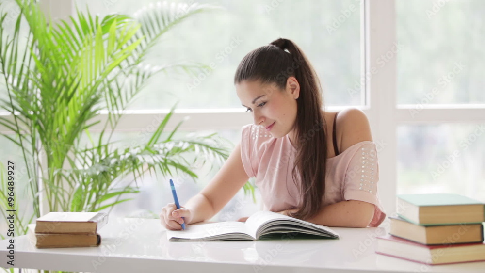 Pretty student girl studying at table with books and smiling at camera Pretty student girl studying at table with books and smiling at camera