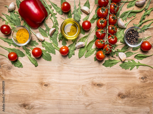 horizontal border with vegetables   oil  cherry tomatoes on a branch  pepper  seasoning  arugula  garlic border  with text area on wooden rustic background top view