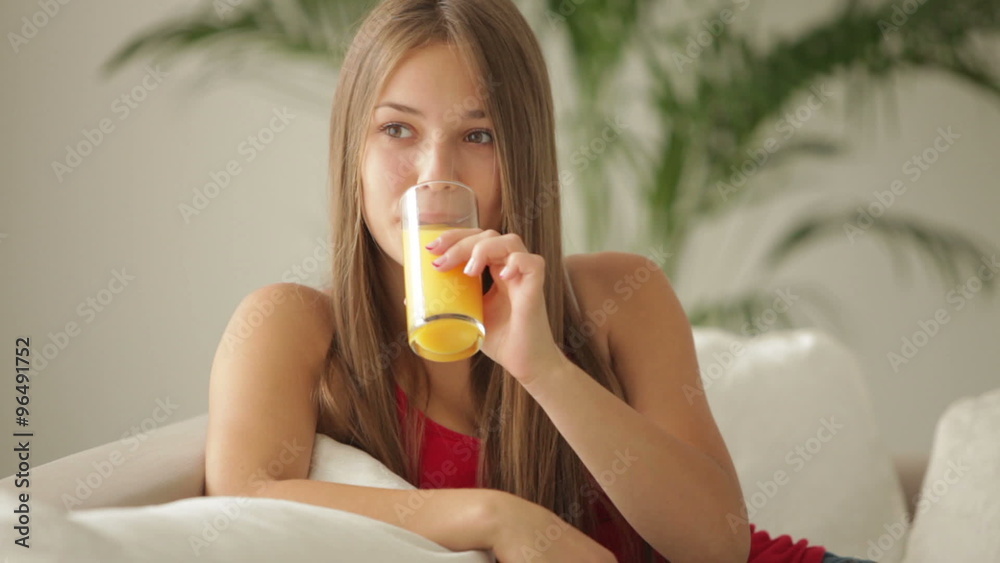 Beautiful girl sitting on sofa drinking juice and smiling