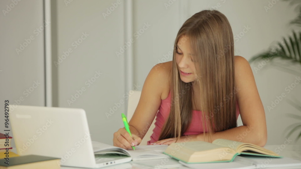 Charming girl sitting at table and studying with books and laptop Charming girl sitting at table and studying with books and laptop