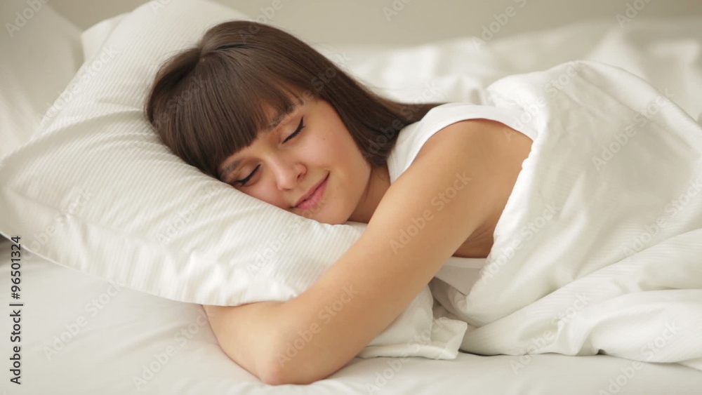 Cute girl sleeping in bed opening her eyes and smiling