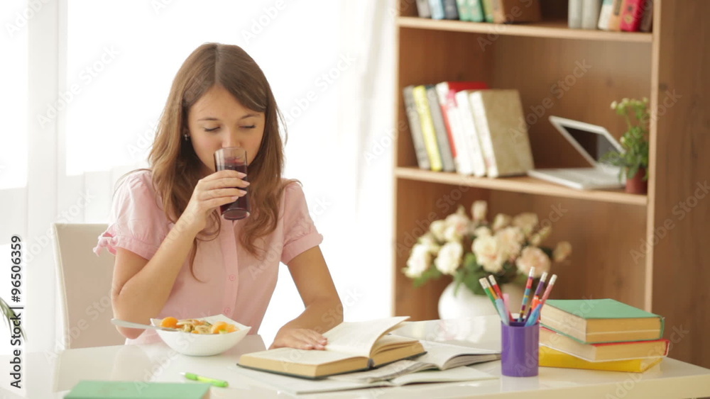 Cheerful girl sitting at table studying drinking juice and smiling at camera Cheerful girl sitting at table studying drinking juice and smiling at camera