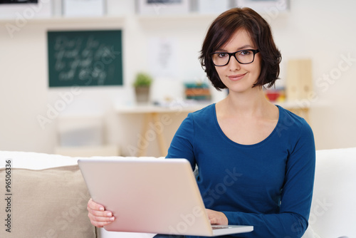 lächelnde frau sitzt auf dem sofa und arbeitet am notebook