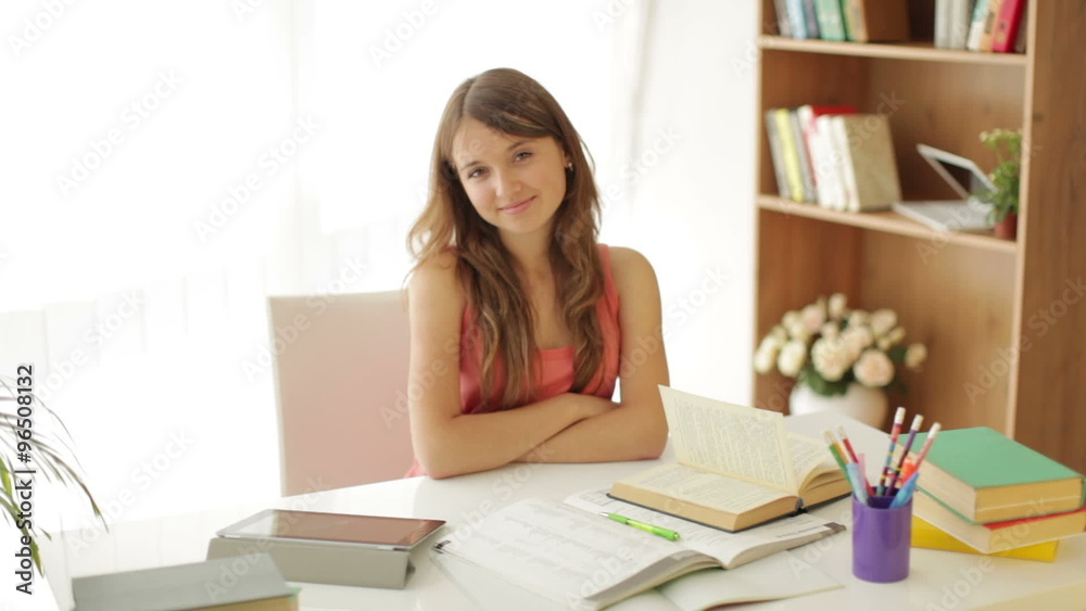 Cute sitting at table with books and touchpad looking at camera and smiling Cute sitting at table with books and touchpad looking at camera and smiling
