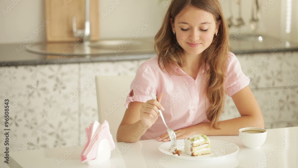 Happy girl sitting at kitchen table eating cake looking at camera and smiling Happy girl sitting at kitchen table eating cake looking at camera and smiling
