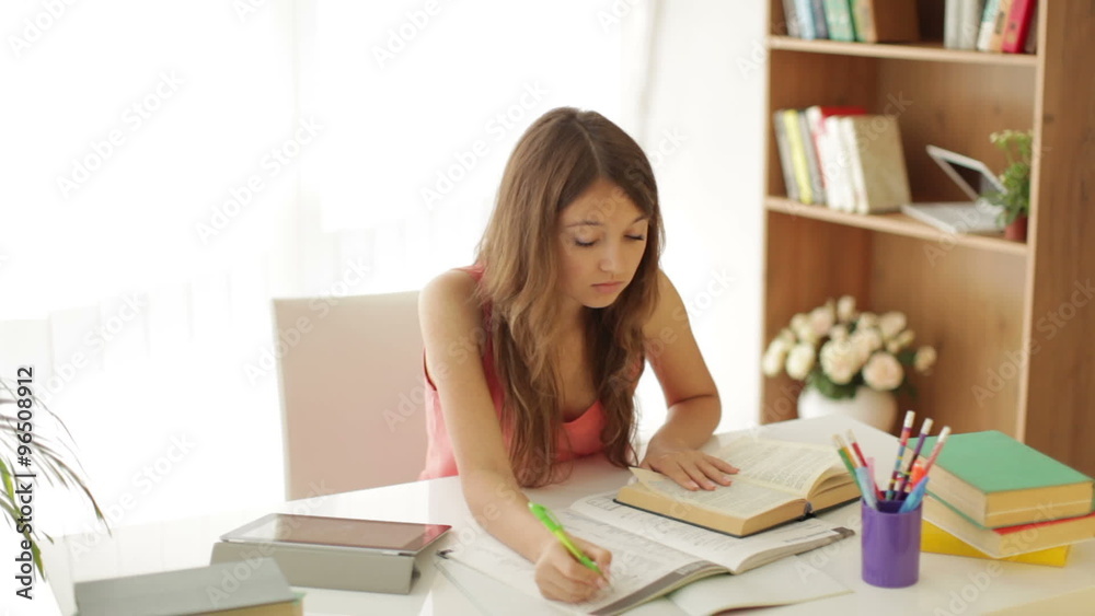 Happy girl sitting at table studying writing in workbook looking at camera and smiling Happy girl sitting at table studying writing in workbook looking at camera and smiling