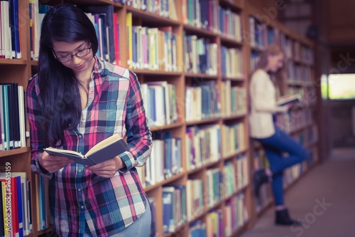 Smiling student leaning against bookshelves reading book