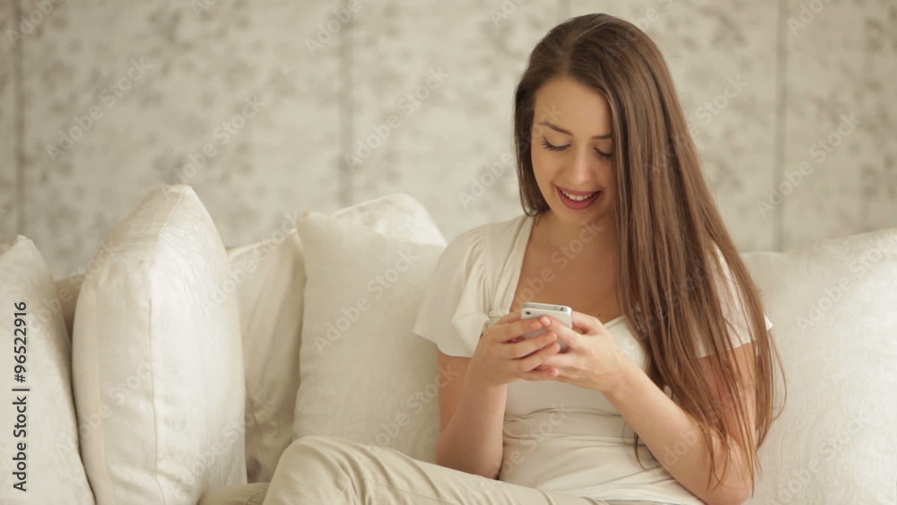 Cute young woman chilling on sofa using mobile phone and smiling at camera Cute young woman chilling on sofa using mobile phone and smiling at camera