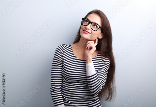Pretty casual thinking woman in glasses looking up on blue backg