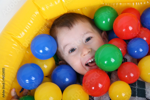 Little smiling boy playing in colorful balls playground