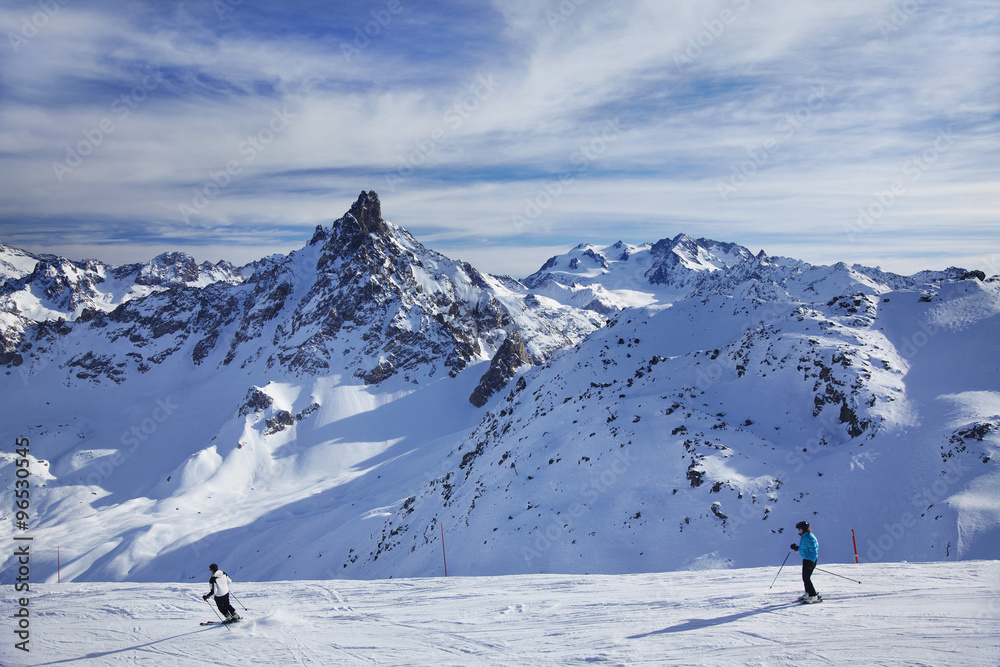 Skiers on a downhill run with mountain backdrop, Three Valleys ski resort, France.