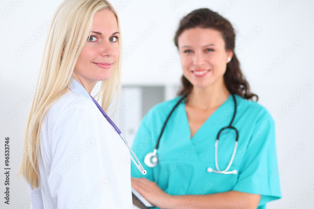 Beautiful young smiling female doctor standing at hospital with doctor on the background. Medical concept. Beautiful young smiling female doctor standing at hospital with doctor on the background. Medical concept.