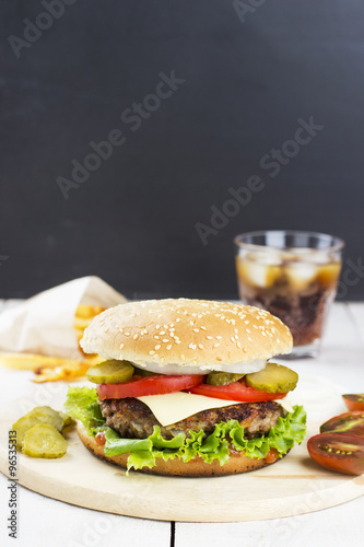 Burger with vegetables, french fries and drink on a wooden backg
