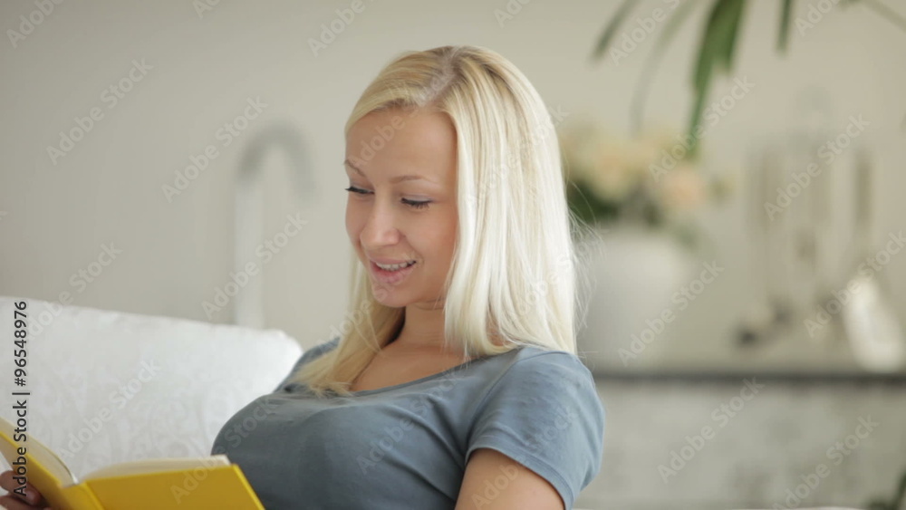 Cute girl sitting on sofa with book closing it and smiling at camera Cute girl sitting on sofa with book closing it and smiling at camera