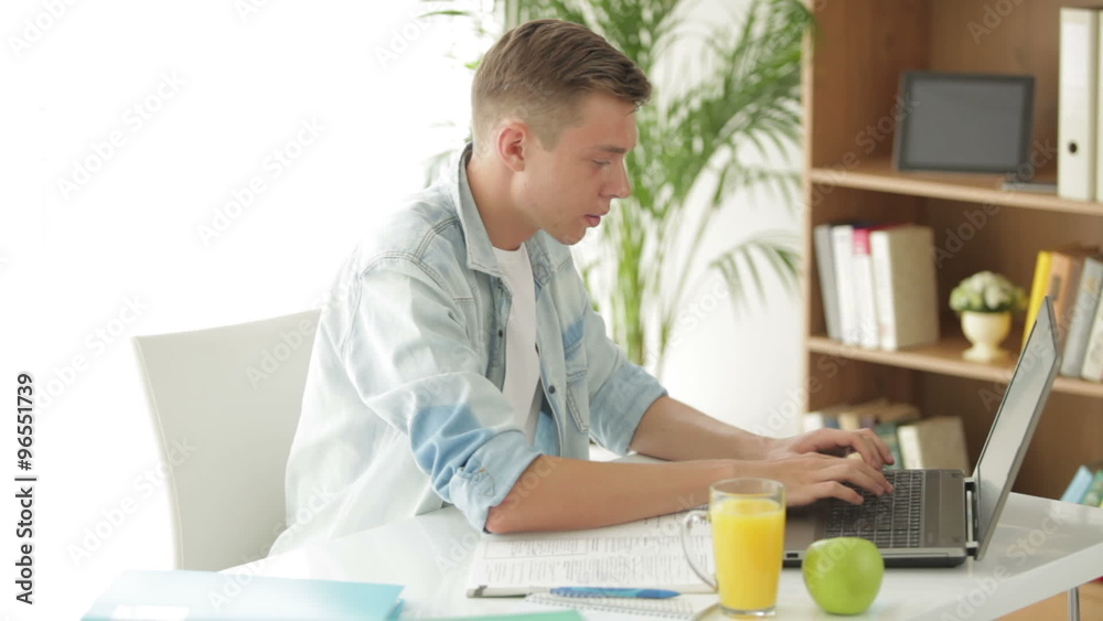 Attractive man sitting at table writing in notebook and using laptop Attractive man sitting at table writing in notebook and using laptop