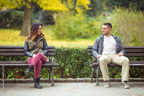 Two young people sitting on benches in a park and talking photo