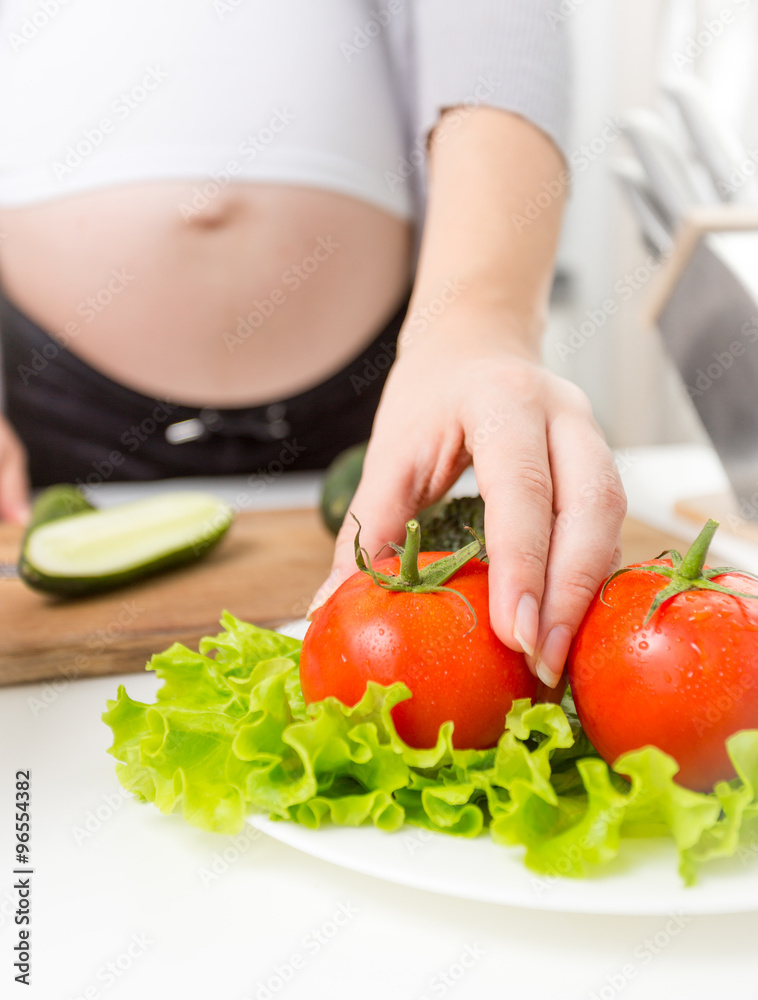 Closeup of pregnant woman taking fresh tomato from plate Closeup of pregnant woman taking fresh tomato from plate